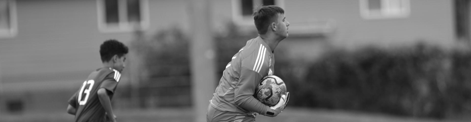 Goalie with the ball with a player running in the background